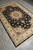 Full length diagonal photo of the 5'9" x 8'9" black Tabriz rug on grey flooring
