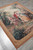 Flat weave pictorial rug photographed from the corner, rose pink and sage green garden scene