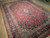 Angled floor view of large 10x13 red Kashan rug, navy guard borders and dense floral field