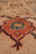 Macro angle of rust rosette with teal petals, showing hand-knotted wool pile and knot structure