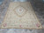 Rug laid flat on travertine tile, angled view showing cream field and plain camel outer border