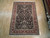 Rug laid flat on pale wood floor, black ground and burgundy border seen from above