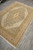 Rug photographed lengthwise from a corner, medallion foreshortened against pale grey floor tiles