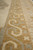 Border detail at low angle: camel ground with cream hooked scrollwork and grey cross motifs