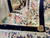 Rug corner folded back on grey tile, showing border roses, selvage and fringe