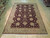 Rug laid flat on pale wood floor, dark red field and cream fringe at near end