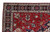 Close corner view showing ivory guard border, navy rosette band and angular floral drawing on red ground