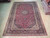 Rug laid flat on pale wood flooring, seen lengthwise with rolled carpets stacked either side
