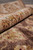 Rolled edge of the rug resting on the pile, border flowers and brown field visible