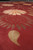 Close low angle detail of carved olive leaf and peach daisy against deep burgundy wool pile