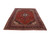 Angled view of red wool Kashan rug showing dense floral field and navy multi-border frame