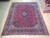 9'10" x 12' Persian Kashan rug displayed on light wood showroom floor beside stacked rugs
