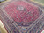 10x12 Persian Kashan rug photographed at an angle revealing plum red field and navy borders