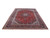 Angled full view of hand-knotted Kashan wool rug showing red field and deep navy main border