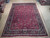 9'4" x 12'8" Mashad Persian rug laid flat on a warehouse floor beside rolled inventory