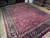 9x13 red Mashad rug photographed at an angle showing dense wool pile and ivory guard borders