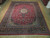 Angled warehouse view of the 10x13 red Persian rug with ivory fringe and black border