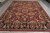 Hand-knotted wool rug laid flat on grey floor showing burgundy field and black border