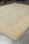 Perspective view of 9x12 sage green Ziegler rug on grey plank floor with ivory fringe