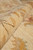 Rolled edge of the rug showing dense wool pile, plush handle and gold vine detail