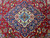Navy lobed medallion anchoring the red Kashan field, framed by curling vines and small blue blossoms
