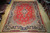 Angled showroom view of a 10x13 red Sarouk rug showing navy border and floral field