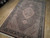 5'9" x 8'10" wool Oriental rug angled across showroom floor, dense Mahi fish pattern visible