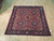 Rose-red and navy Sarouk square rug photographed at an angle on light wood flooring