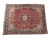 Angled studio view of red and navy hand-knotted Kerman rug with ivory guard borders