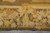 Border close-up showing fruit, blossoms and a masked face motif in yellow and olive tones