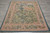 6' x 7' hand woven tapestry rug photographed top down, pink floral border framing leafy green field