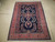 Room size navy area rug laid flat, salmon floral border framing an open blue field