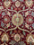 Close-up of gold 8 petal rosette surrounded by serrated vines on wine red field