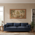 Landscape tapestry hung above a navy sofa in a bright living room with bookshelves