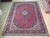 9'10" x 13' Persian Kashan rug laid flat on hardwood showroom floor with red field