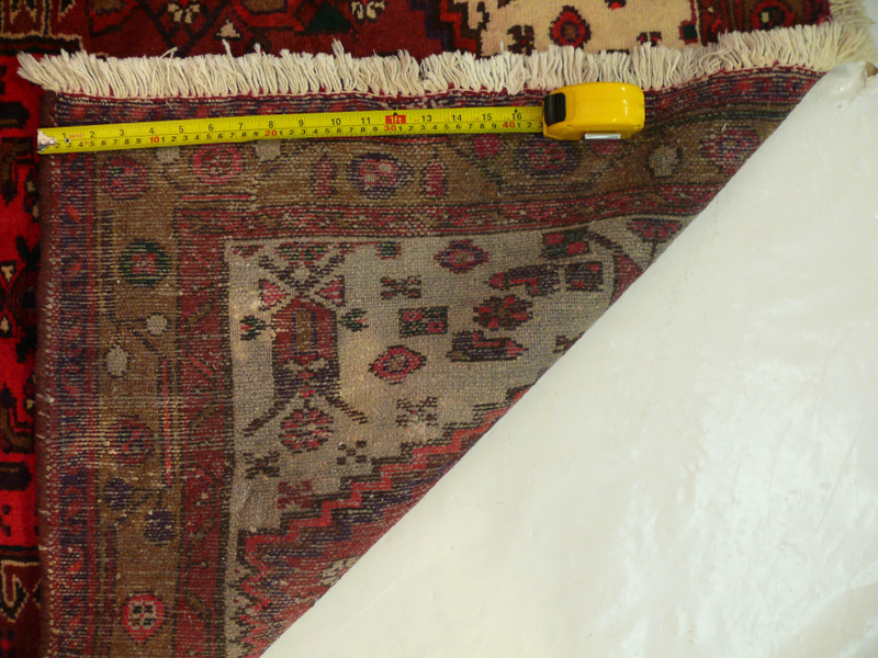 Backside of an antique Persian Hamedan tribal rug shown with a ruler measuring knot density, highlighting tight hand-knotted structure and traditional village weaving quality