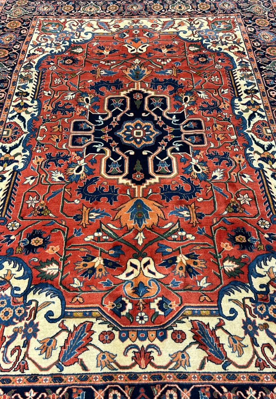 Midfield detail of a geometric Persian Heriz rug showing floral motifs, angular vines, and saturated red background