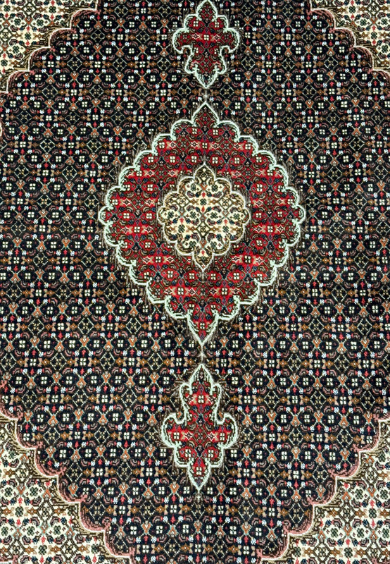 Detailed image of the central medallion of a Persian Tabriz Mahi rug, with red, navy blue, and cream details on a dark brown base