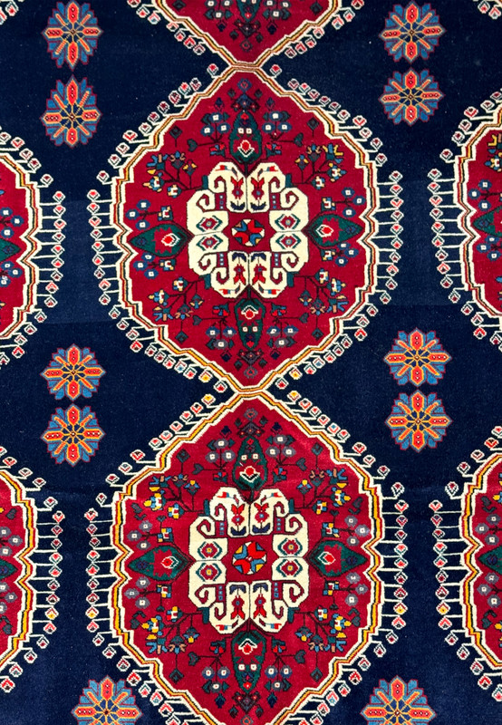 Close-up of the intricate design of a Persian Qashqai rug featuring diamond-shaped medallions with floral motifs in a rich color palette on a dark blue background