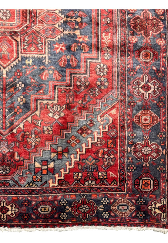 Partial view of a vintage Persian Bijar rug showing the edge and corner designs, featuring detailed floral and geometric patterns in red, blue, and cream