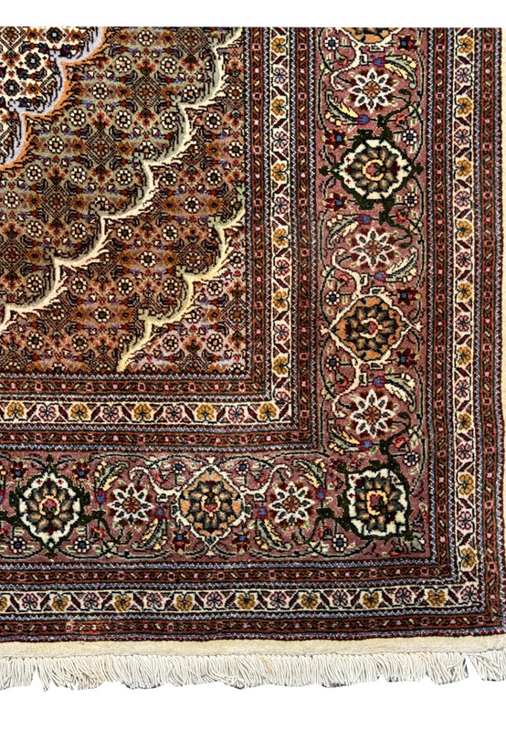 Close-up of the 5x7 Persian Tabriz Mahi rug's border, featuring detailed floral and geometric patterns in a variety of colors on a dark base, bordered by cream fringe.
