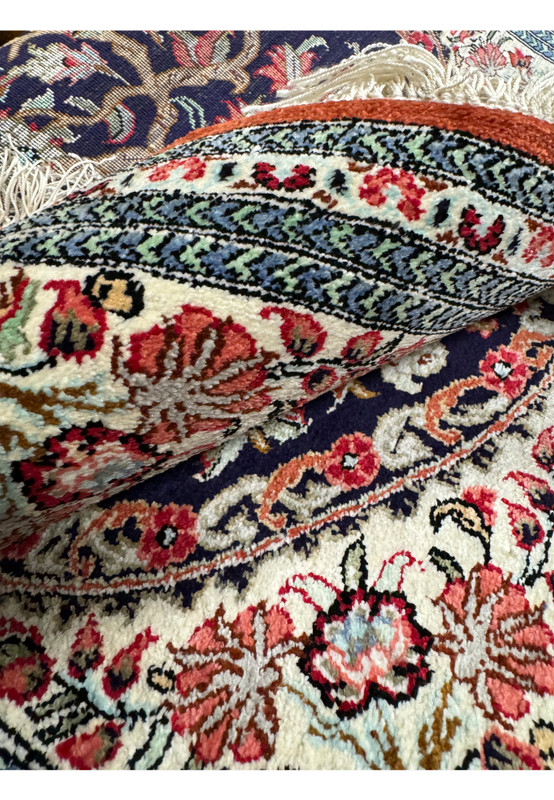 Folded corner of the Persian Qum silk rug revealing the rug's thickness and the intricate design continuity