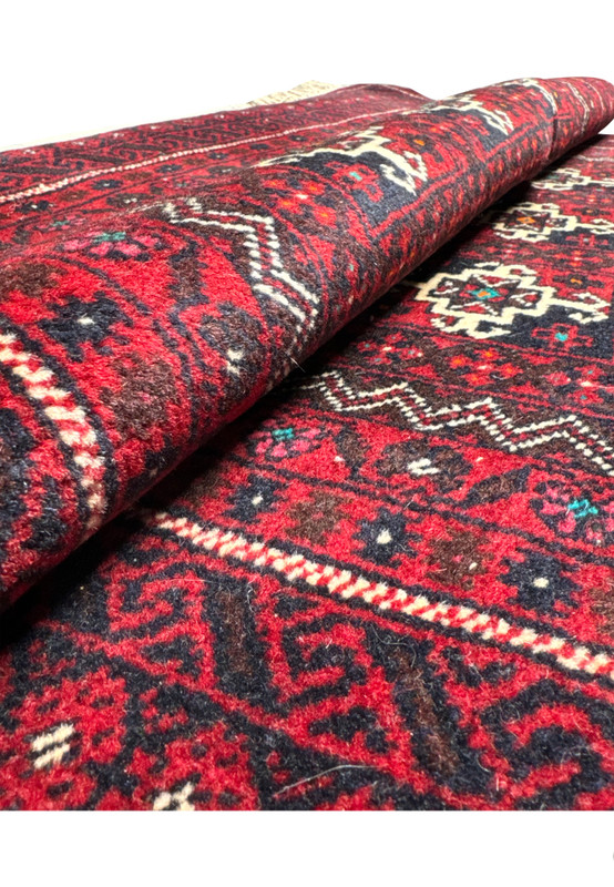 Folded Persian Baluch rug, revealing the texture and weave pattern, along with the depth of color variation in reds and blues