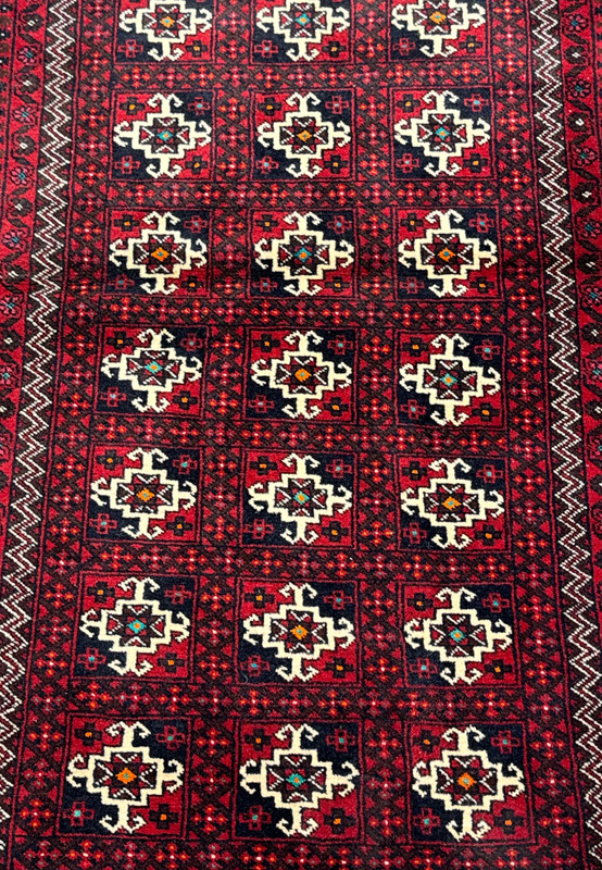 Close-up of a Persian Baluch rug showcasing detailed patterns with dark red, white, navy, and hints of green and orange