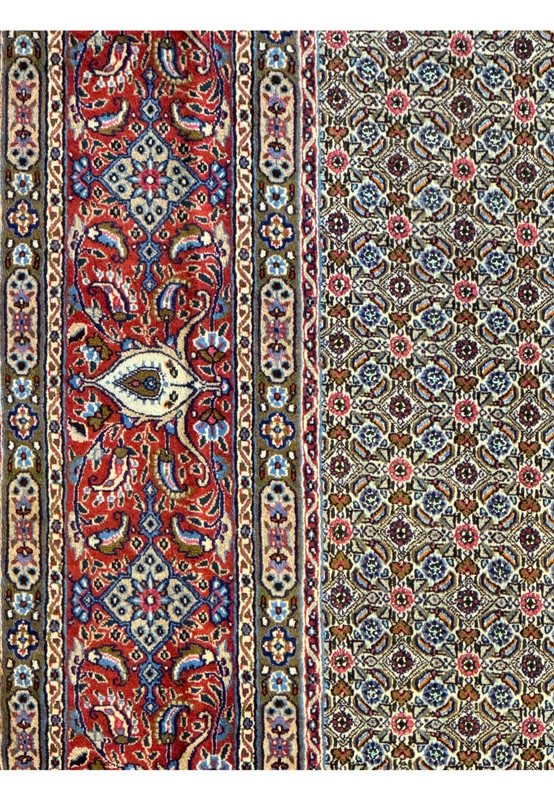 Detailed shot of the Persian Moud Rug's border featuring ornate floral designs and prominent medallions against a deep red backdrop