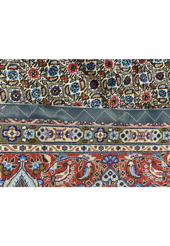 A detailed view of the Persian Moud Rug's backside, showcasing the tight weave and the reverse pattern, with a section of the rug's front and the leather anti-slip strip visible
