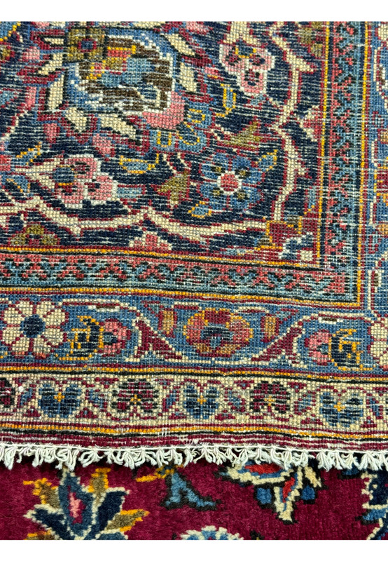 Edge detail of a Persian Kashan rug highlighting the fine craftsmanship of the border patterns against the plush burgundy pile