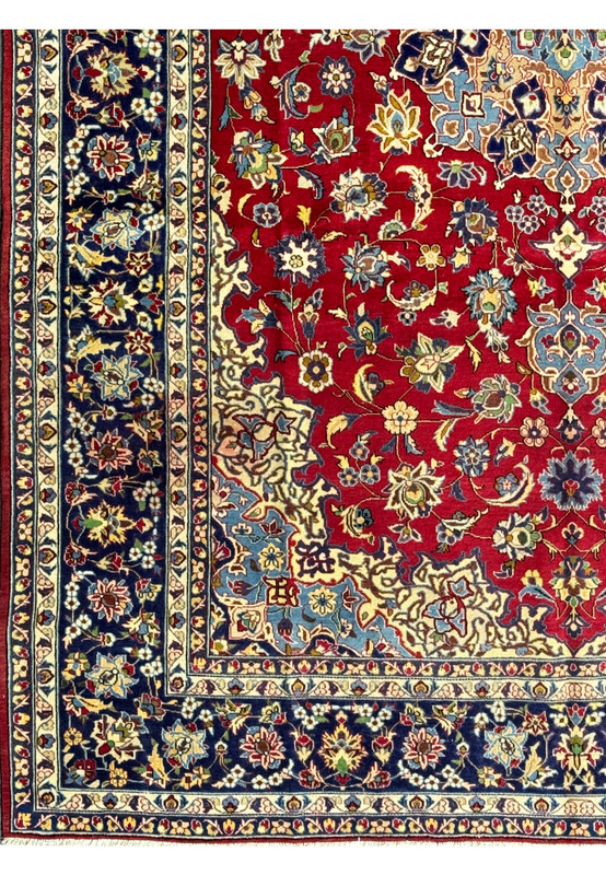 A close-up of the Persian Isfahan rug's border and part of the central field, showing the fine details of the floral motifs and the contrasting colors of the navy border against the red background