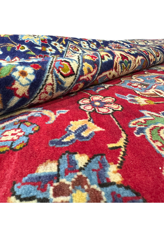 A 10 x 15'6" Persian Isfahan rug partially rolled, displaying the detailed patterns and vivid colors on the intricate border and the plush red field