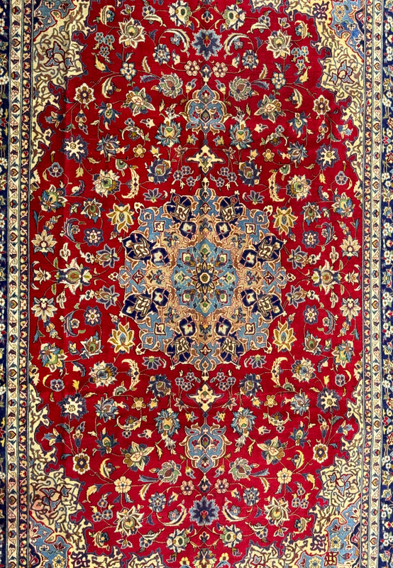 A close-up view of the central part of a Persian Isfahan rug, highlighting the elaborate central medallion and the detailed floral patterns in colors of blue, gold, and white on a red background